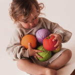 Toddler with an arm full of various Oli & Carol 100% Natural Rubber Baby Sensory Balls