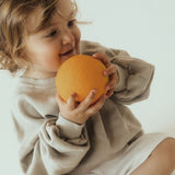Toddler holding the Oli & Carol 100% Natural Rubber Baby Sensory Ball - Orange
