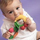 Baby chewing on Oli & Carol Natural Rubber Baby Teething Ring - Fruit with a purple background