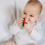 Close up of a baby chewing the oli and carol natural rubber soft baby teething toy on a white bed