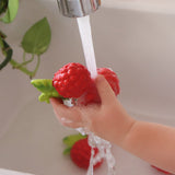 Close up of a childs hand holding the oli and carol soft rubber raspberry food toy under a running tap