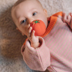 A baby clutching onto a tomato ball from the Oli & Carol Veggie Salad Baby Sensory Balls set.