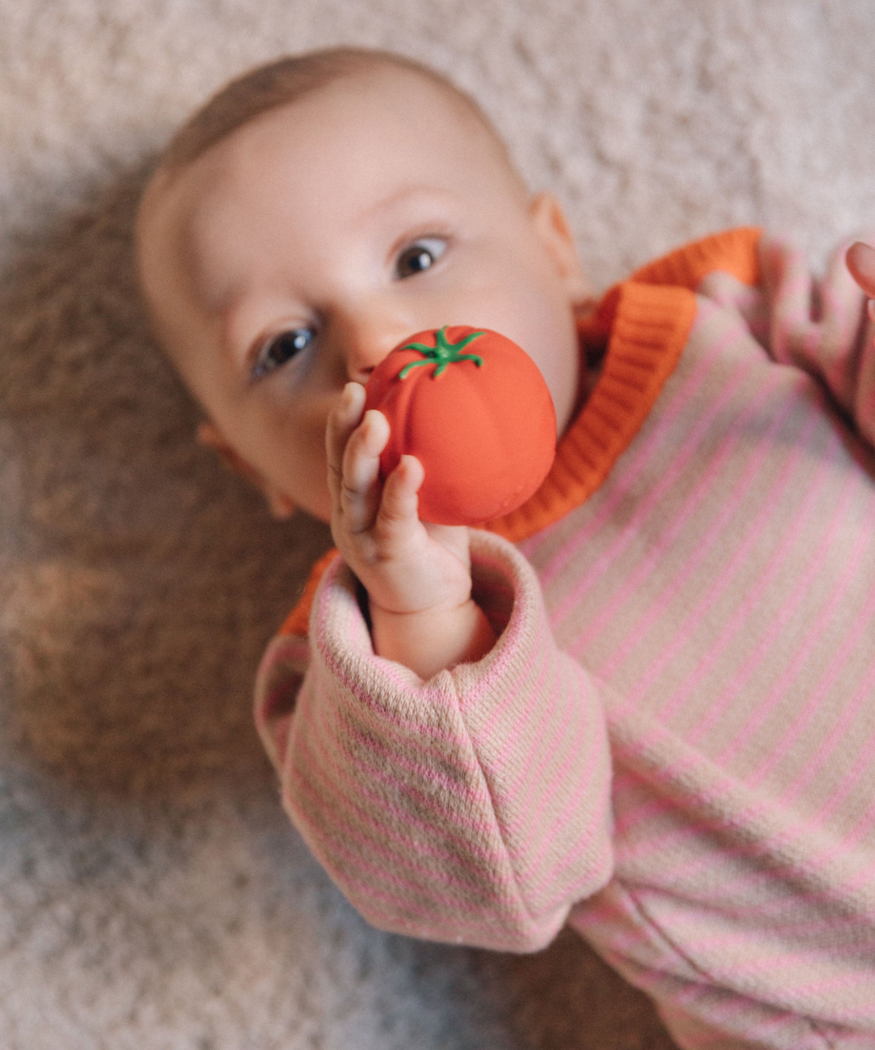 A baby clutching onto a tomato ball from the Oli & Carol Veggie Salad Baby Sensory Balls set.