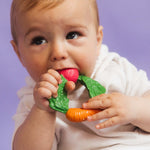 A baby clutching the Oli & Carol Natural Rubber Veggie Teething Ring.