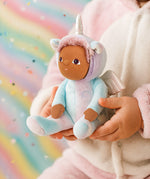 Olli Ella Dinky dinkum doll Uli Unicorn available at Babipur. Close up of soft cuddly doll held by a child with a glittery rainbow background.  