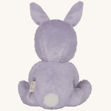 Olli Ella purple coloured Babs Bunny Dinky Dinkum Doll in a seated position facing away from the camera showing the back of the doll. A white fluffy tail can be seen. 