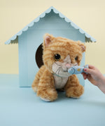 A close up of a child's hand holding the magnetic blue fish in front of the Olli Ella Koda dinkum cat doll available at Babipur