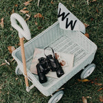 Black binoculars and a map inside the Olli Ella classic blue wonder wagon toy on some grass