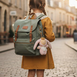 The back of a little girl on an empty European street, wearing a backpack with an Olli Ella Bunny Flopsy bag charm attached.