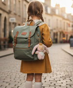 The back of a little girl on an empty European street, wearing a backpack with an Olli Ella Bunny Flopsy bag charm attached.