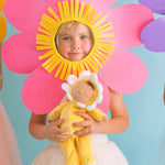 A child wearing a big pink flower headdress holding on to a Olli Ella Buttercup Pip Dozy Dinkum Doll.