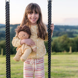 Young girl stood next to a rope swing holding an Olli Ella dinkum doll dressed in the goldie striped pyjamas