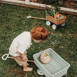 Boy hunched over collecting eggs in a basket inside the Olli Ella blue rattan wagon on some grass