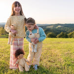 Two young girls stood in a grass field holding some Olli Ella dozy dinkum doll toys dressed in the goldie stripe pyjamas