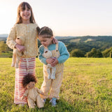 Two young girls stood in a grass field holding some Olli Ella dozy dinkum doll toys dressed in the goldie stripe pyjamas