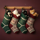 A festive photo featuring Olli Ella binky kitten toy dolls sitting inside a Christmas stocking handing on hooks. These soft dolls are available at Babipur.