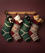 A festive photo featuring Olli Ella binky kitten toy dolls sitting inside a Christmas stocking handing on hooks. These soft dolls are available at Babipur.