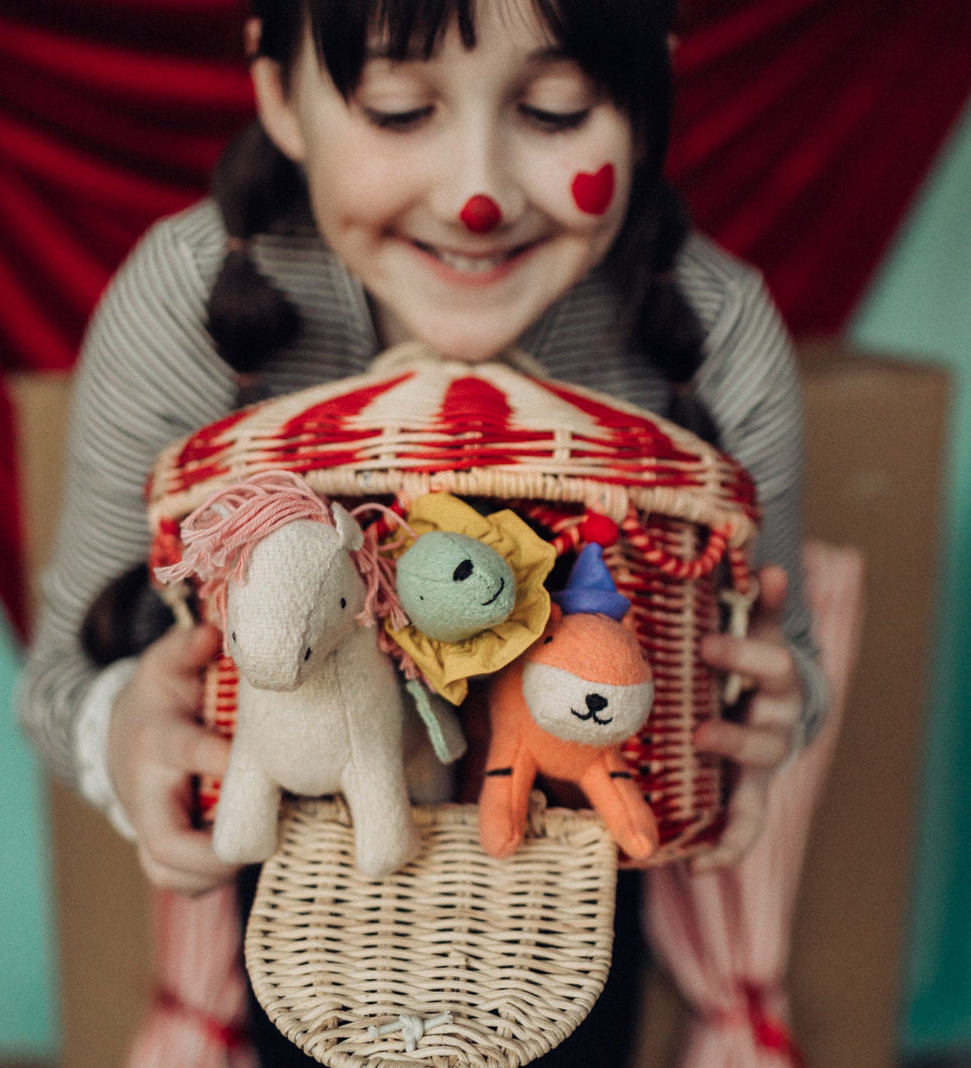 A child holding the Olli Ella red and white rattan basket filled will holdie folk animal dolls poking through the door available at Babipur. 