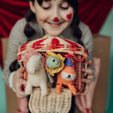A child holding the Olli Ella red and white rattan basket filled will holdie folk animal dolls poking through the door available at Babipur. 
