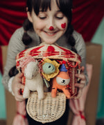 A child holding the Olli Ella red and white rattan basket filled will holdie folk animal dolls poking through the door available at Babipur. 