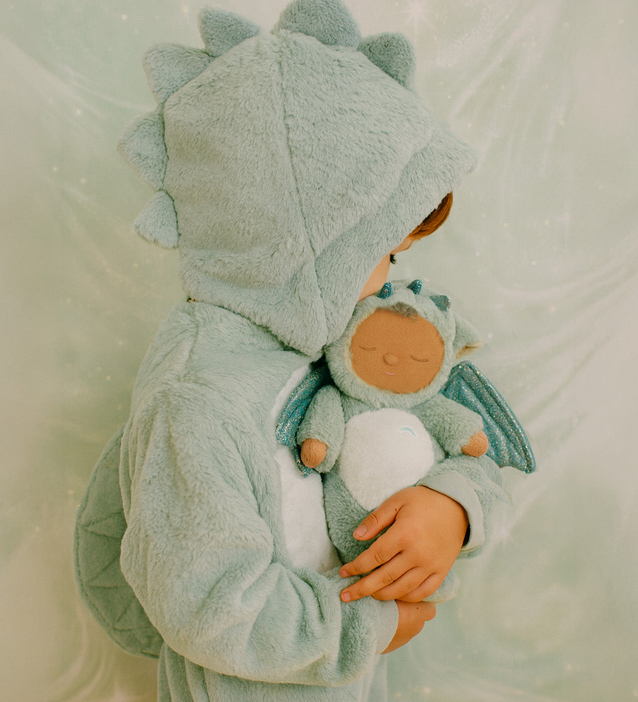 A child wearing a dragon outfit and holding the Olli Ella Ash cozy dinkum doll