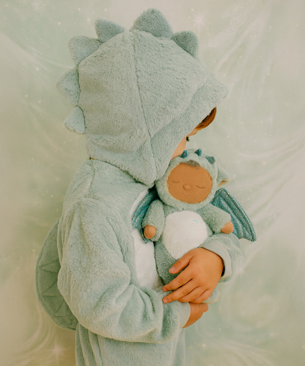 A child wearing a dragon outfit and holding the Olli Ella Ash cozy dinkum doll