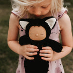 Olli Ella Cozy Dinkums - Black Cat Nox is held in the hands of a young child.