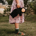 Olli Ella Cozy Dinkums - Black Cat Nox. A child carries Nox by the arm in an outdoor setting