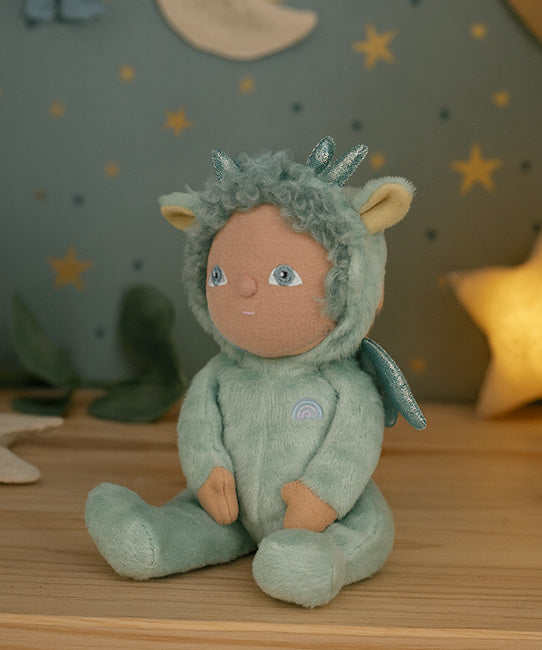 Olli Ella Dante the dinky dinkum dragon doll available at Babipur sitting on a wooden surface with a decorative starry background. 