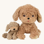 A soft and fluffy Brown Olli Ella Benny puppy sitting next to the Olli Ella dinkum dog on a cream background.