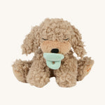 A soft and fluffy Brown Olli Ella Benny puppy with a magnetic dog toy in its mouth on a cream background.