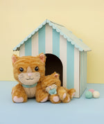 A Olli Ella Binx cat dinkum doll sitting next to koda the binky kitten doll with a cardboard shelter in the background. Both of these soft toy dolls are available at Babipur.
