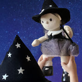 A child holding up an Olli Ella Wendy Witch dream Dinkum doll. A dinkum doll with a black dress, witches hat, black shoes and a magnetic broom accessory. This doll is part of Olli Ella's Halloween collection available here at Babipur.