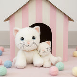 A Olli Ella Lux cat dinkum doll sitting next to Kiki the binky kitten doll with a cardboard shelter in the background. Both of these soft toy dolls are available at Babipur.