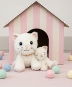 A Olli Ella Lux cat dinkum doll sitting next to Kiki the binky kitten doll with a cardboard shelter in the background. Both of these soft toy dolls are available at Babipur.