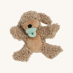 A soft and fluffy Brown Olli Ella Benny puppy with a magnetic dog toy in its mouth on a cream background.