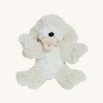 A soft white Olli Ella Belle dinkum puppy with a magnetic dog toy in its mouth on a cream background.