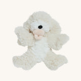 A soft white Olli Ella Belle dinkum puppy with a magnetic dog toy in its mouth on a cream background.