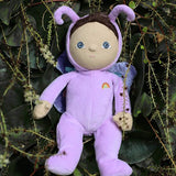 The Olli Ella Dinky Dinkum Doll - Betty Butterfly - in a light purple onesie, with brown hair, blue eyes, dark purple butterfly wings, and antennae. She is in a green leafy bush.