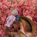 A little girl holding the Olli Ella Dinky Dinkum Doll - Betty Butterfly -in a pink flower garden.