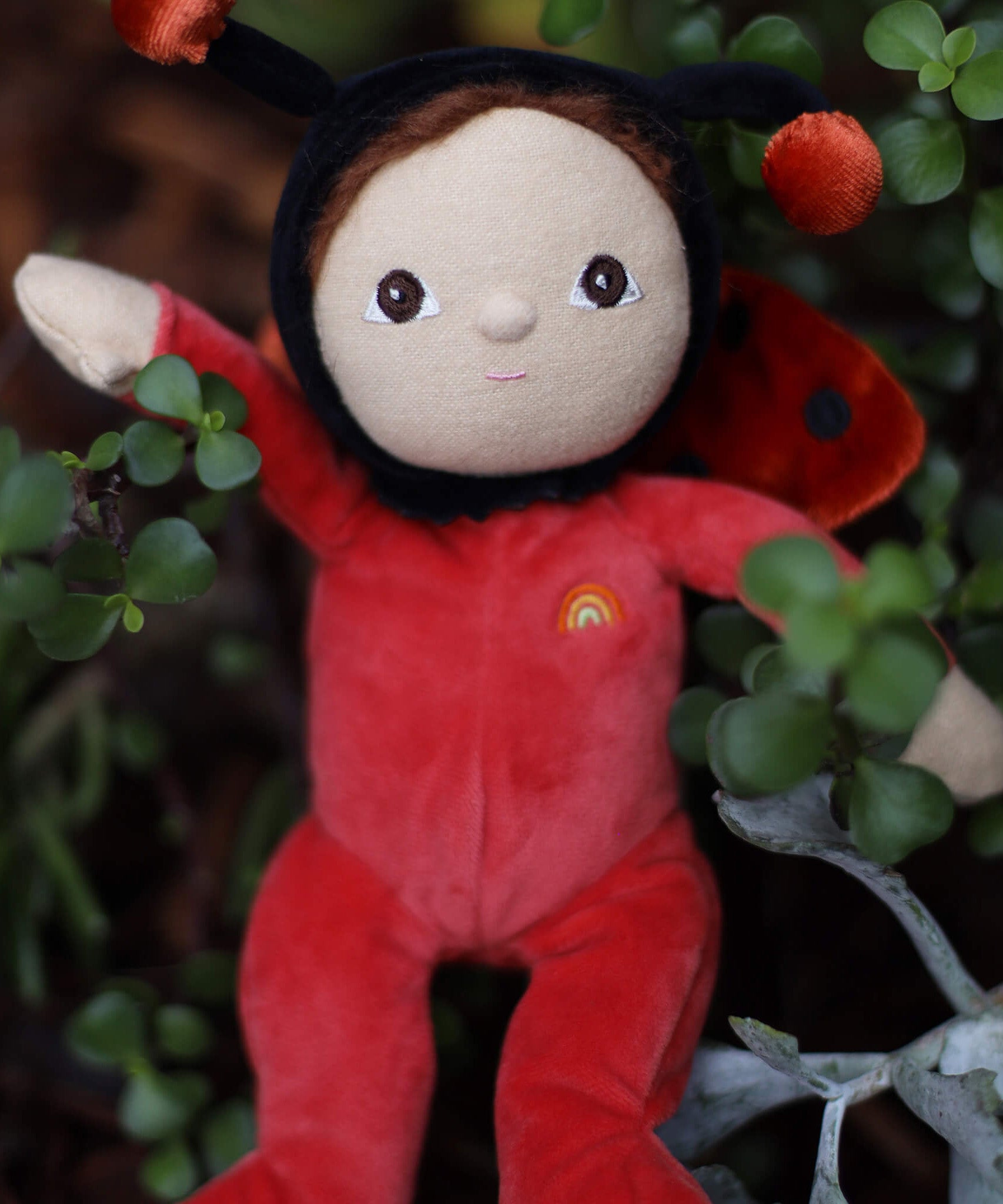 The Olli Ella Dinky Dinkum Doll - Lola Ladybug - in a red onesie with a black hood, brown hair and eyes, spotty ladybird wings, and antennae.