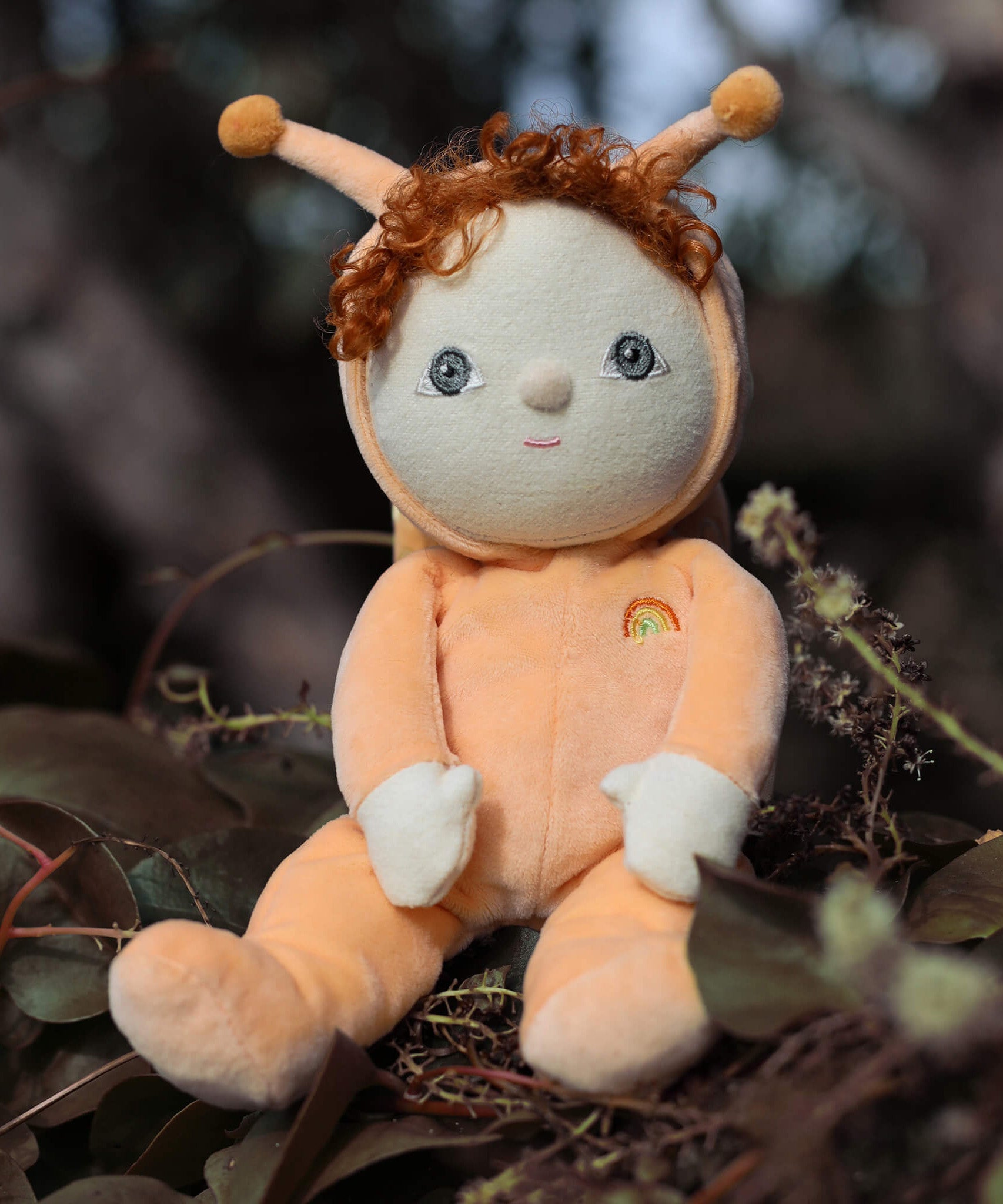 The Olli Ella Dinky Dinkum Doll - Scottie Snail - in a soft light orange onesie with curly red hair, a snail shell on his back, and antennae.