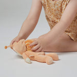 A little girl playing with the Olli Ella Dinky Dinkum Doll - Scottie Snail - in a soft light orange onesie with a snail shell on his back.