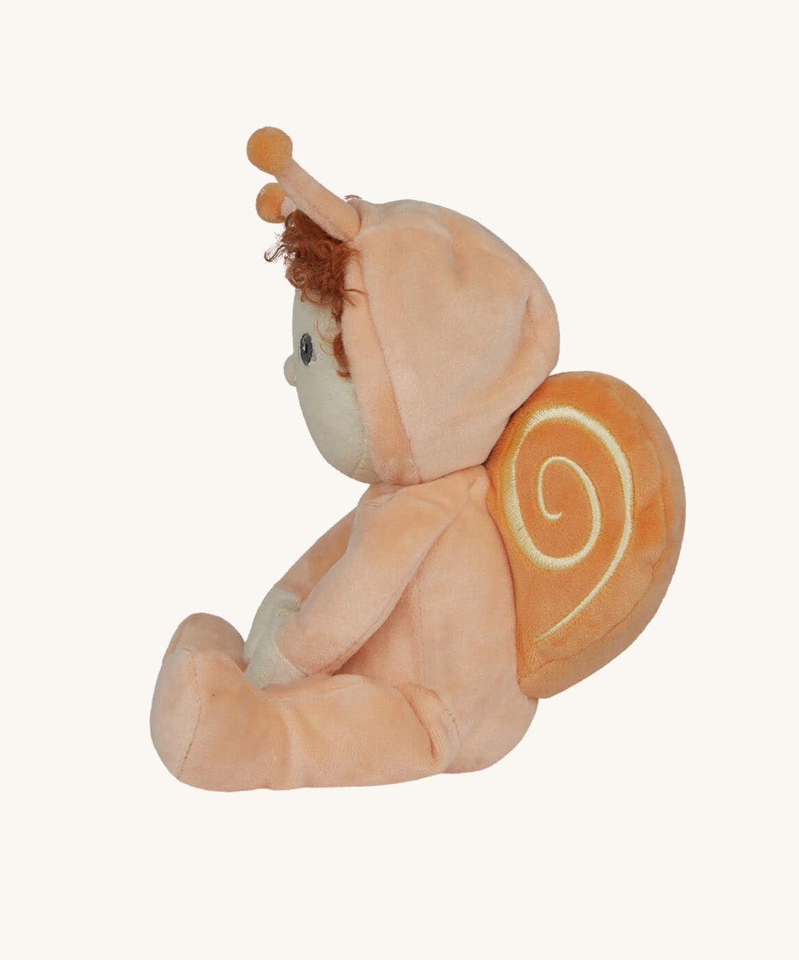 A side profile view of the Olli Ella Dinky Dinkum Doll - Scottie Snail - in a soft light orange onesie with curly red hair, a snail shell on his back, and antennae.