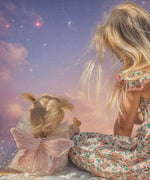 A chid sitting next to the Olli Ella Willow dream dinkum doll available at Babipur and facing a dream starry night sky