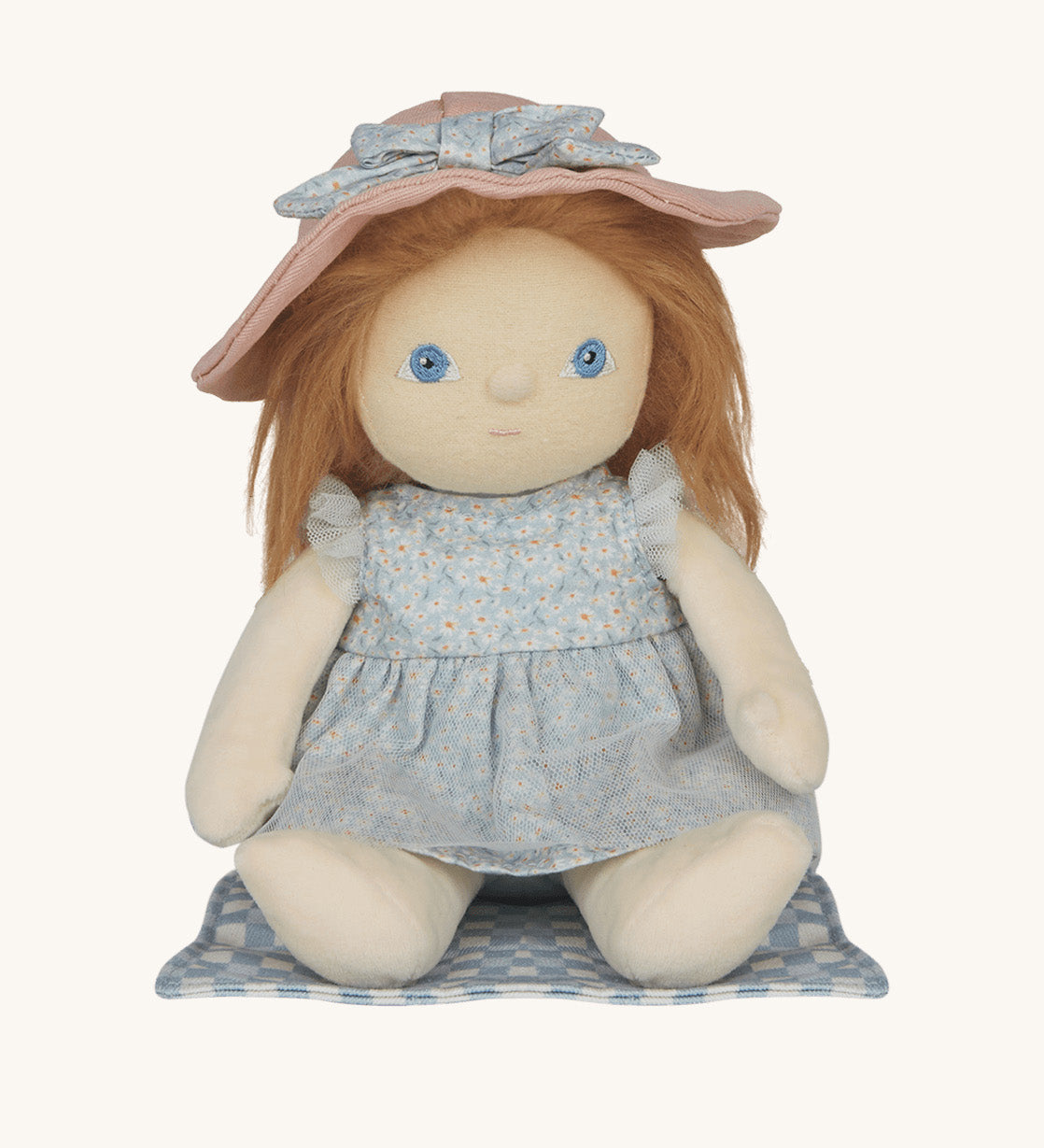 Penelope Petals Dinky Dinkum Doll sitting on her gingham picnic blanket, wearing floral blue dress and pink sunhat from Olli Ella’s Dress Me range.