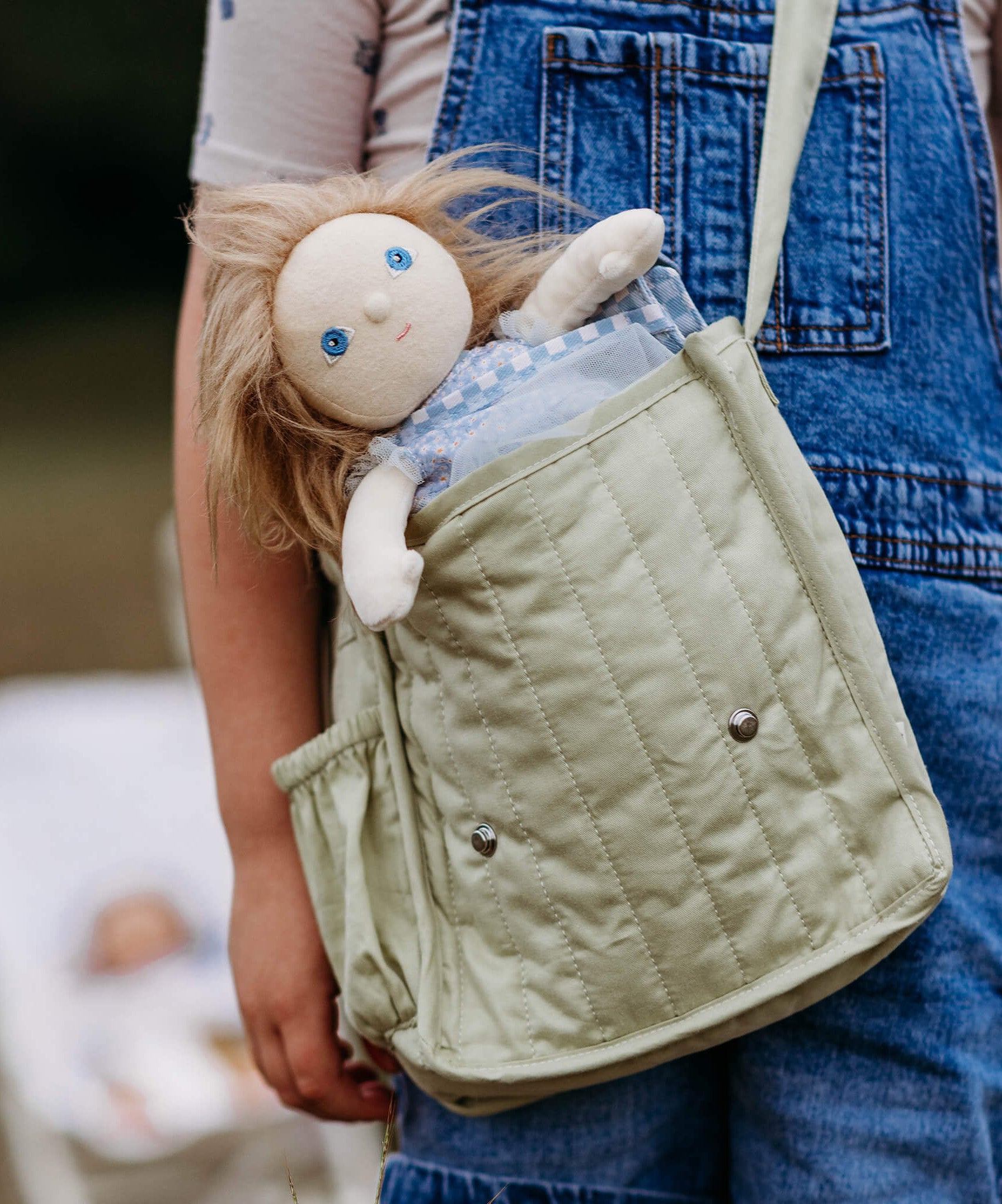 Penelope Petals Olli Ella Dinky Dinkum Doll tucked into a child’s shoulder bag, showing her long hair, soft body, and dress-up outfit.
