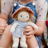 Olli Ella Dress Me Dinky Dinkum Doll Penelope Petals held by a child, showing her blue floral dress, pink sunhat, and soft posable design.