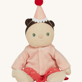 Olli Ella Dress Me Dinky - Sophie Sundae, a doll with brown hair and green eyes wearing a pink polka dot dress, light pink cardigan and a pink party hat. Sat down, cream background.