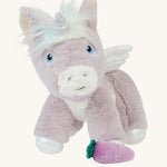 The Olli Ella Glimmer unicorn, which has light purple fur and a white mane with pastel coloured streaks, with a purple carrot at its feet